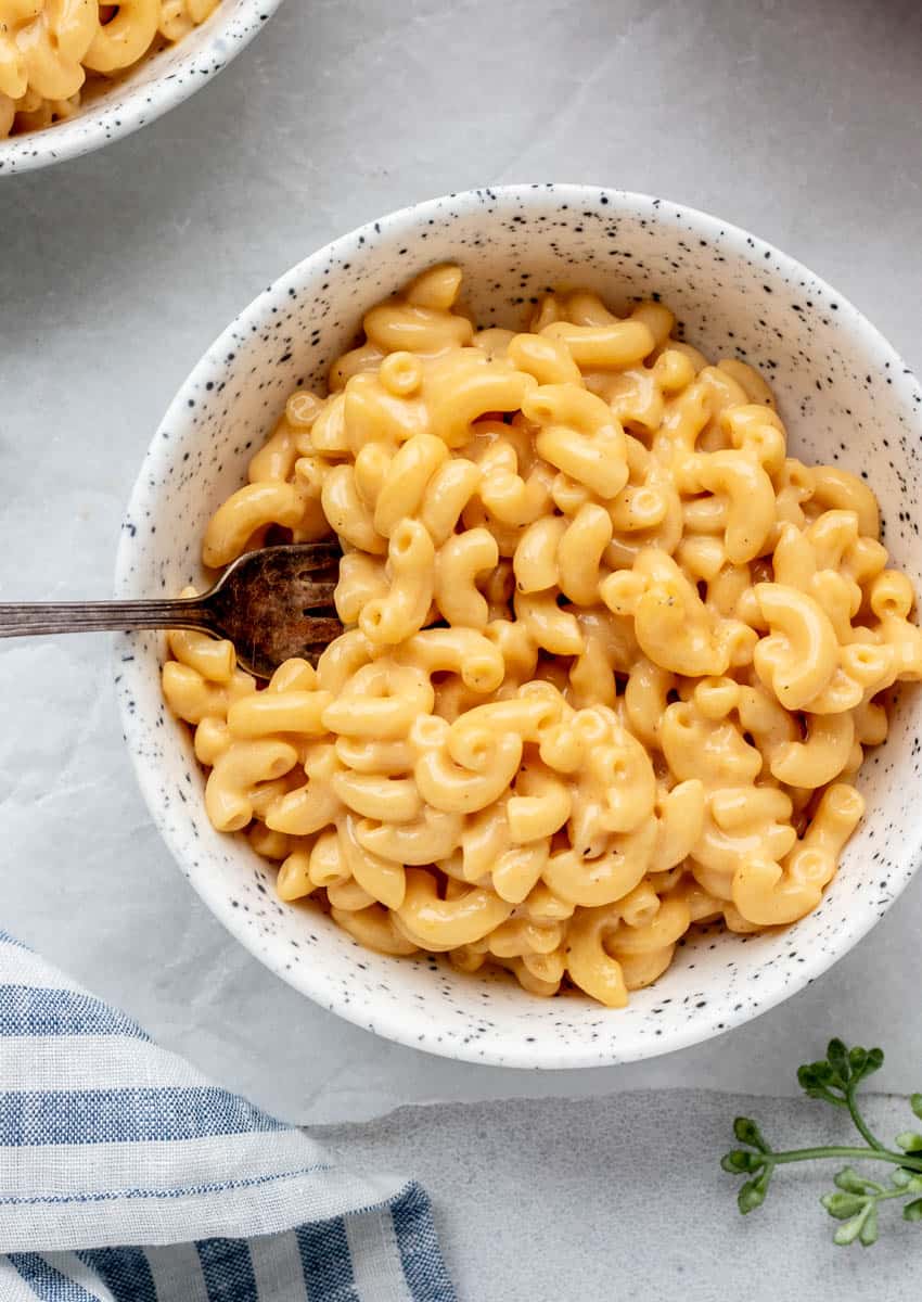 A closeup view of no flour mac and cheese in a speckled bowl with a fork.