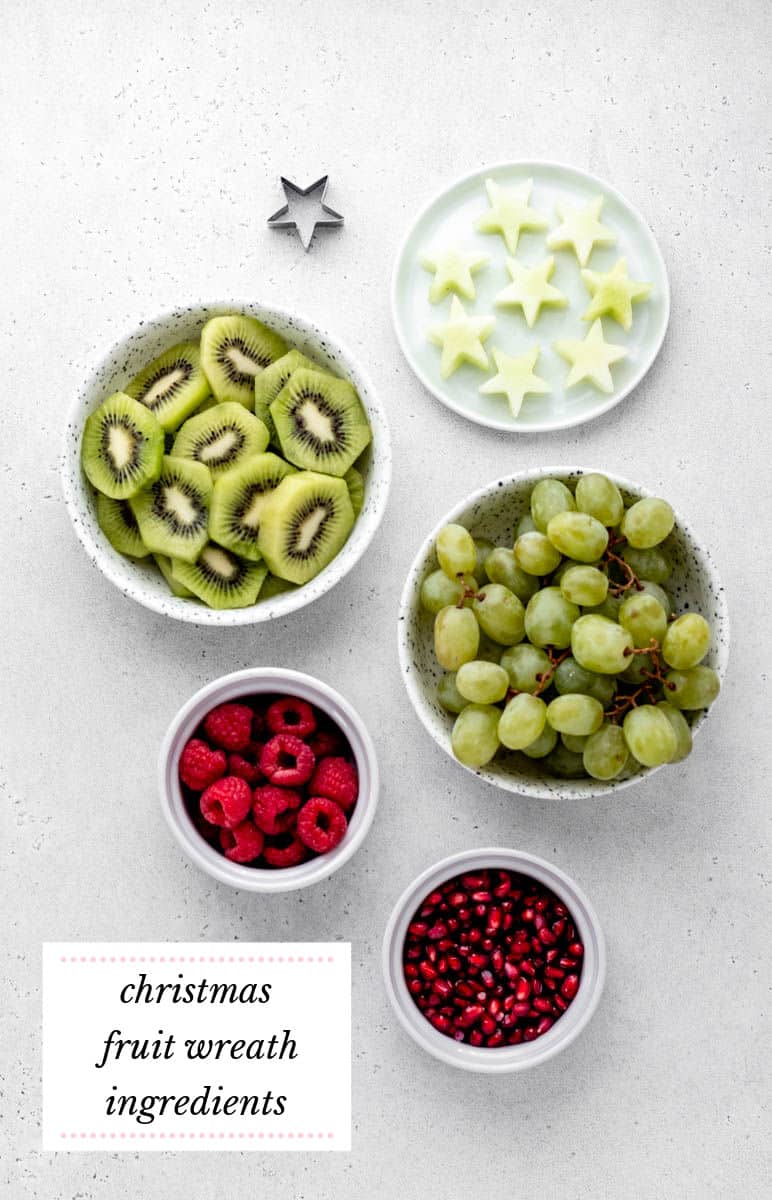 Christmas fruit platter ingredients, including star shaped honey melon, kiwi slices, red grapes and pomegranate arils.
