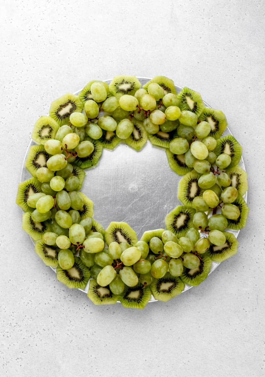 Green grapes fill in the gap between the sliced kiwis on the Christmas fruit tray.