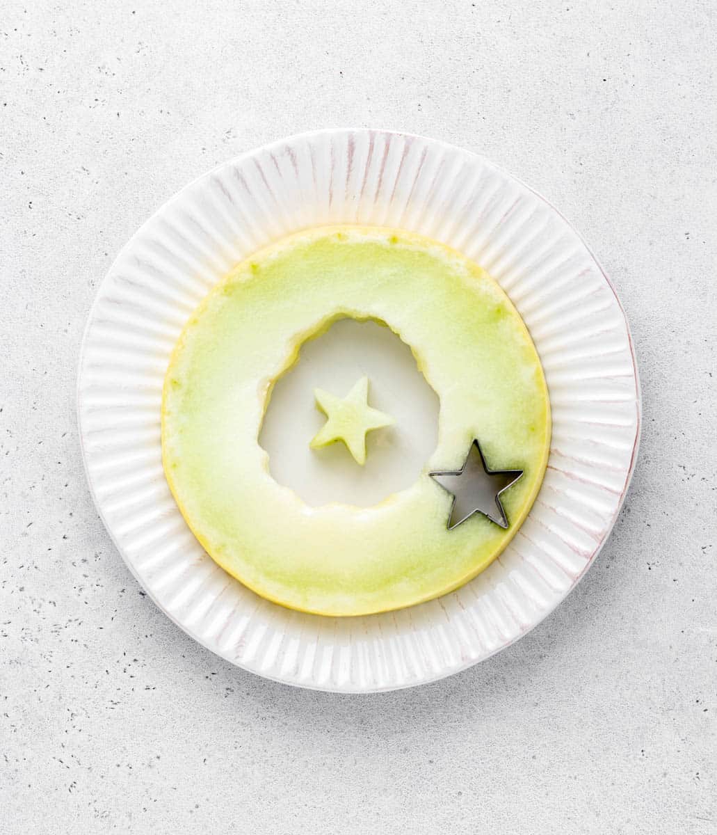 A circular slice of honey melon has a star shape cut out of it.