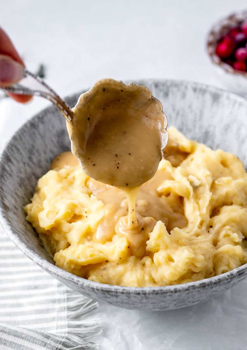 Gravy without drippings being poured over a bowl of mashed potatoes.