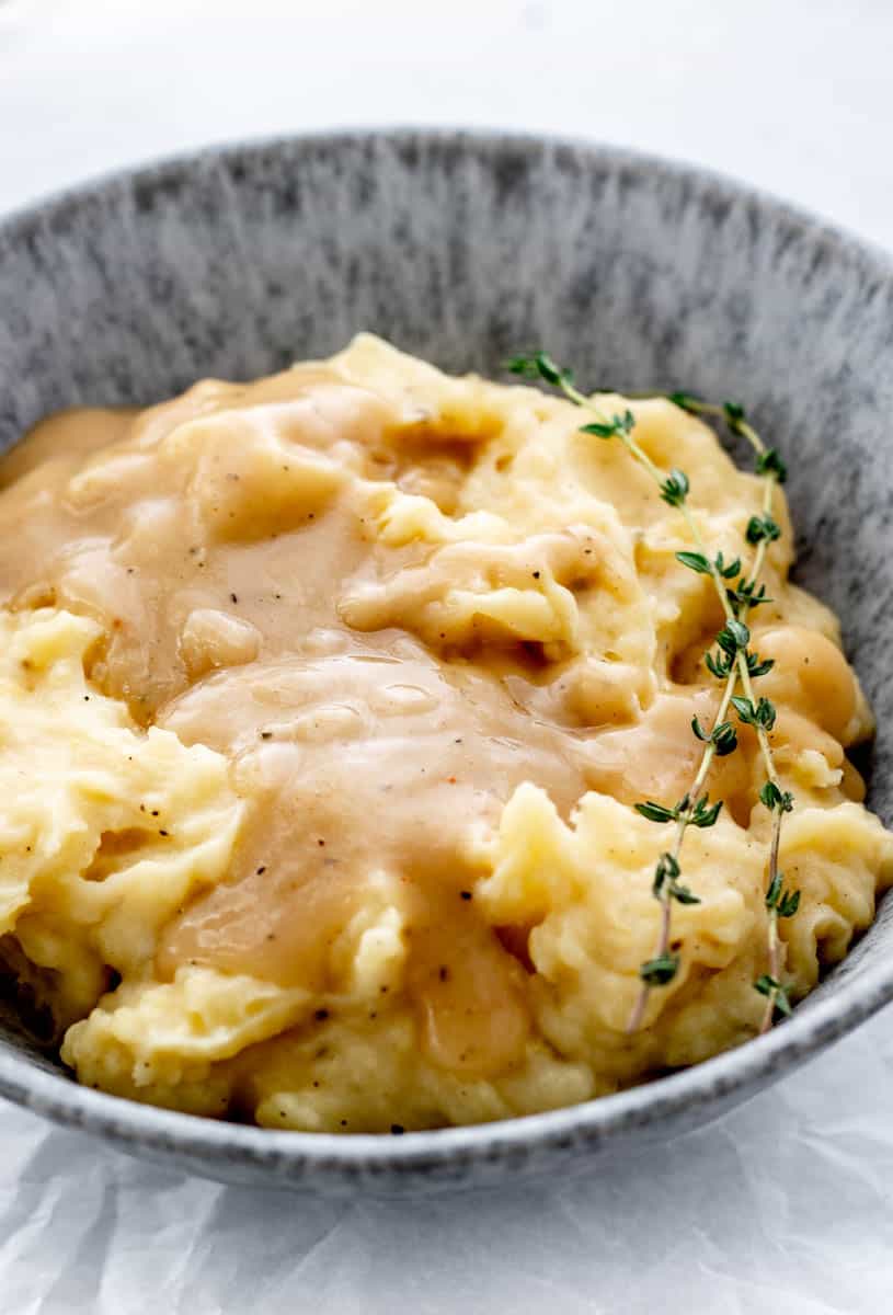 Mashed potatoes topped with gravy and a sprig of thyme.