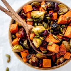A wooden spoon holding a serving of Maple roasted brussel sprouts and sweet potatoes with dried cranberries and pumpkin seeds.