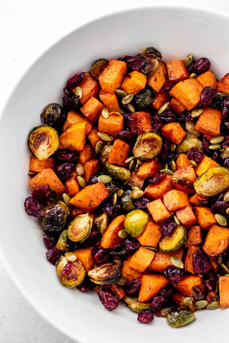 A white bowl with maple roasted brussel sprouts and sweet potatoes with dried cranberries and pumpkin seeds.