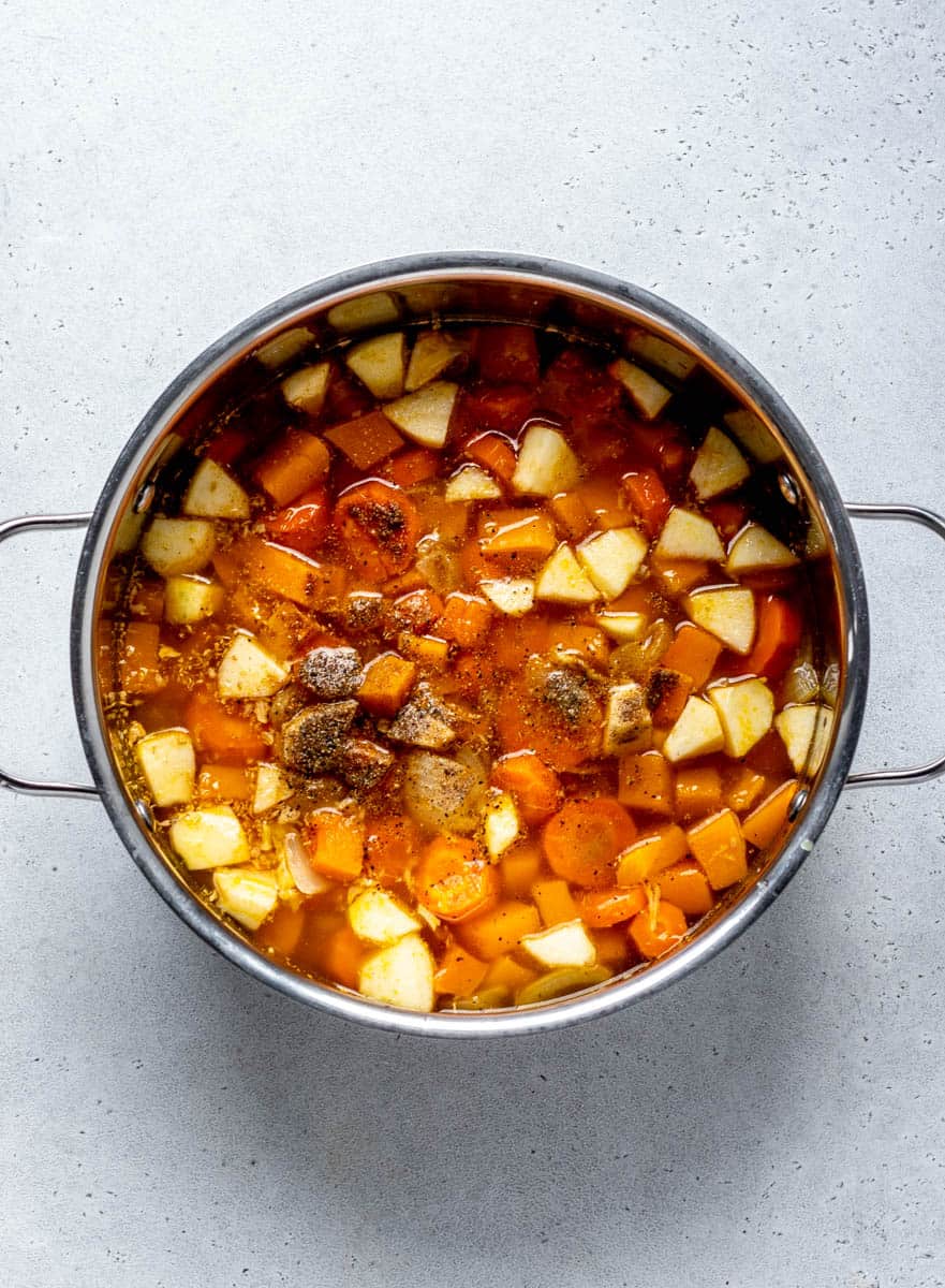 Roasted vegetables, broth, apple, and spices in a large pot.