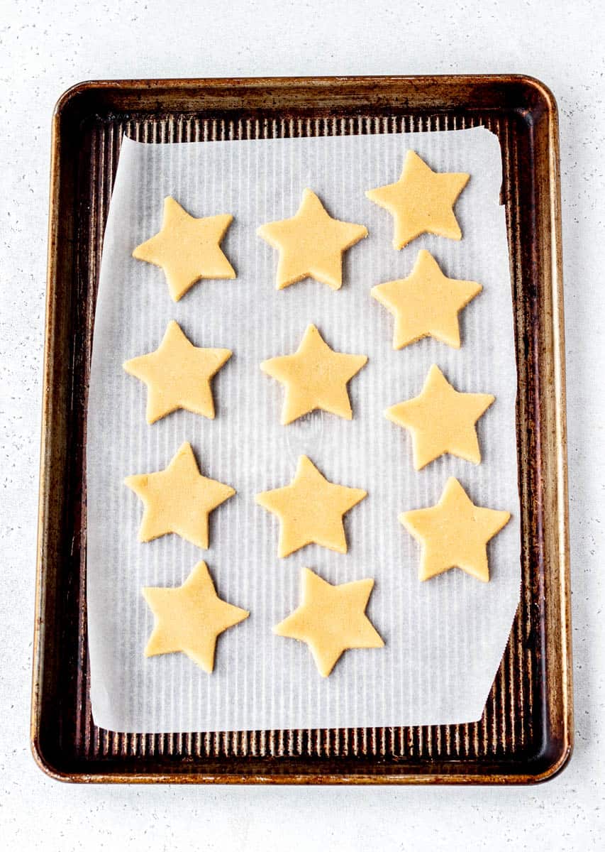 Star cut outs of almond flour cookies on parchment paper, on a baking sheet.