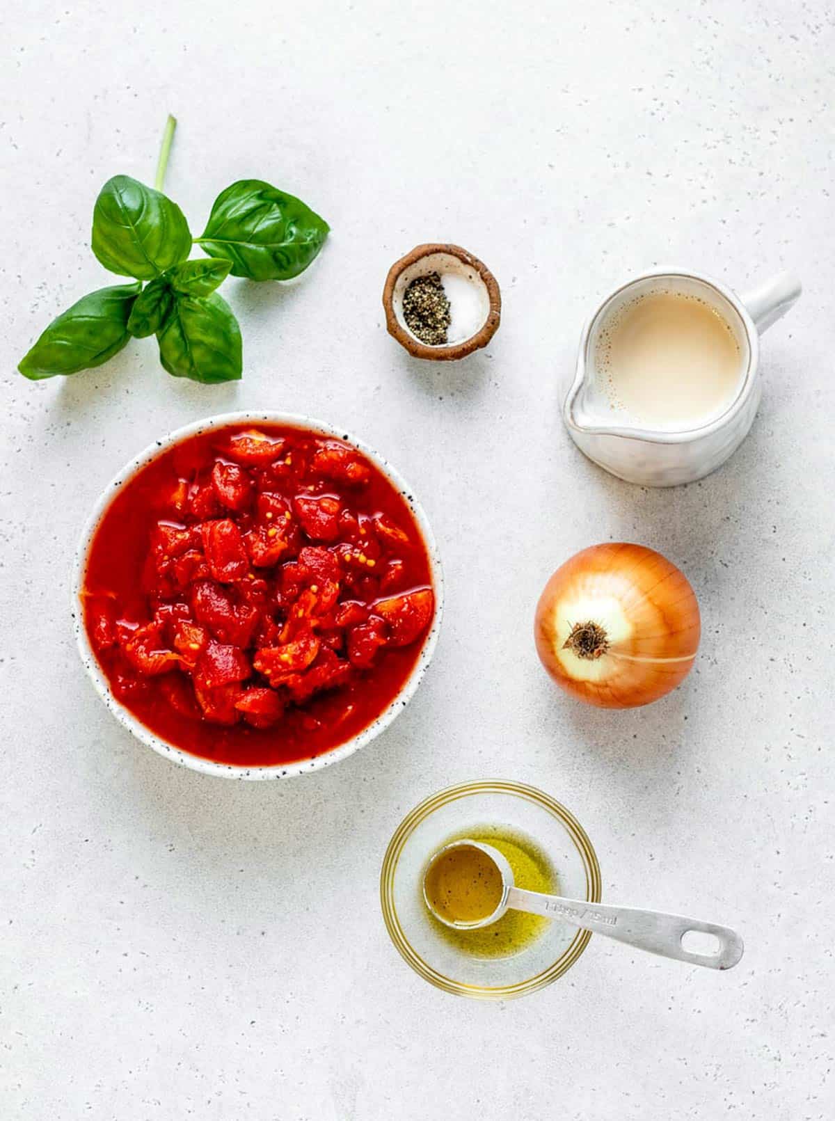 The ingredients for homemade tomato soup, including fresh basil, salt and pepper, evaporated milk, diced tomatoes, onion and olive oil.