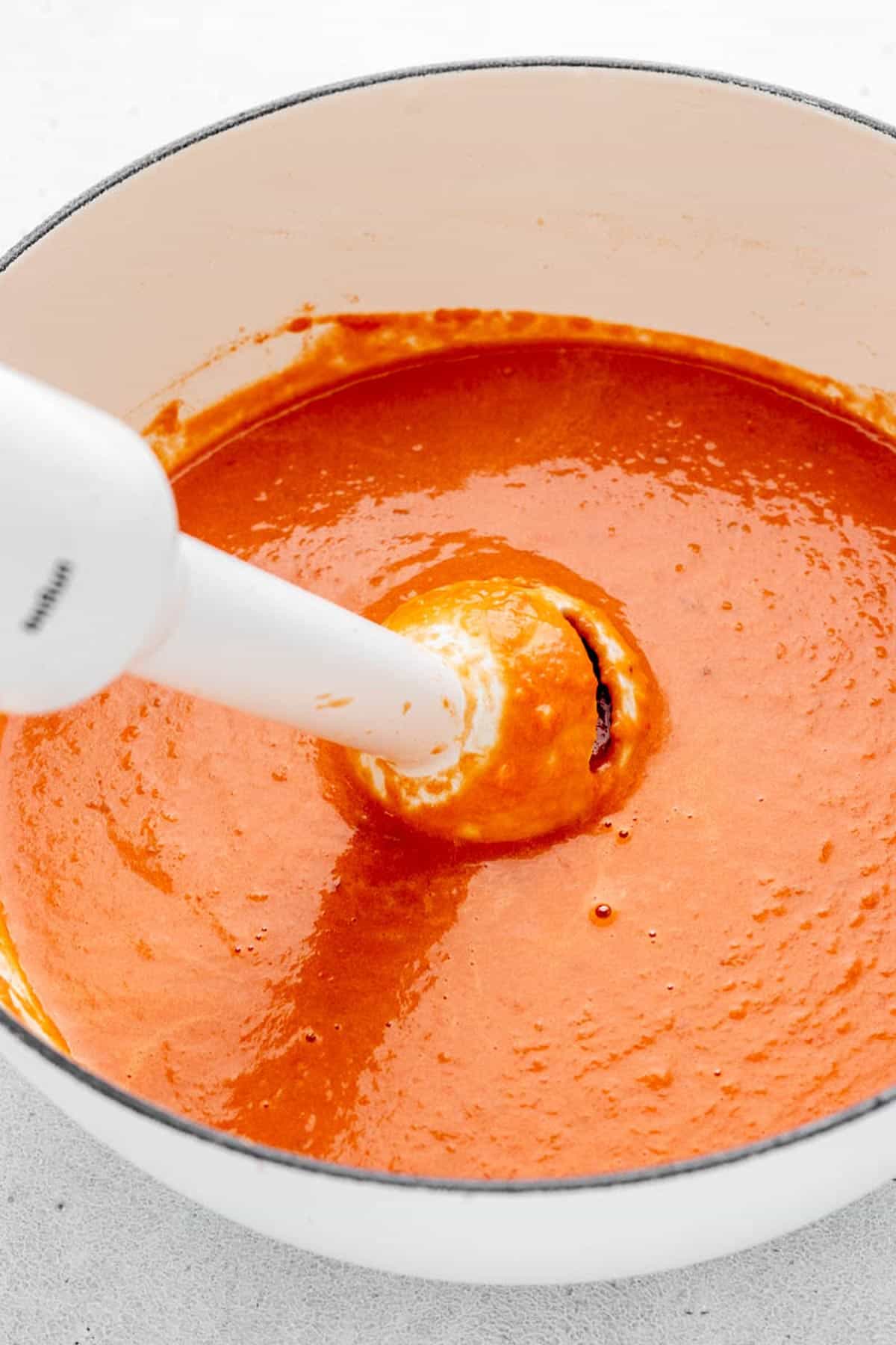 An immersion blender blending the tomato onion soup in the sauce pan.