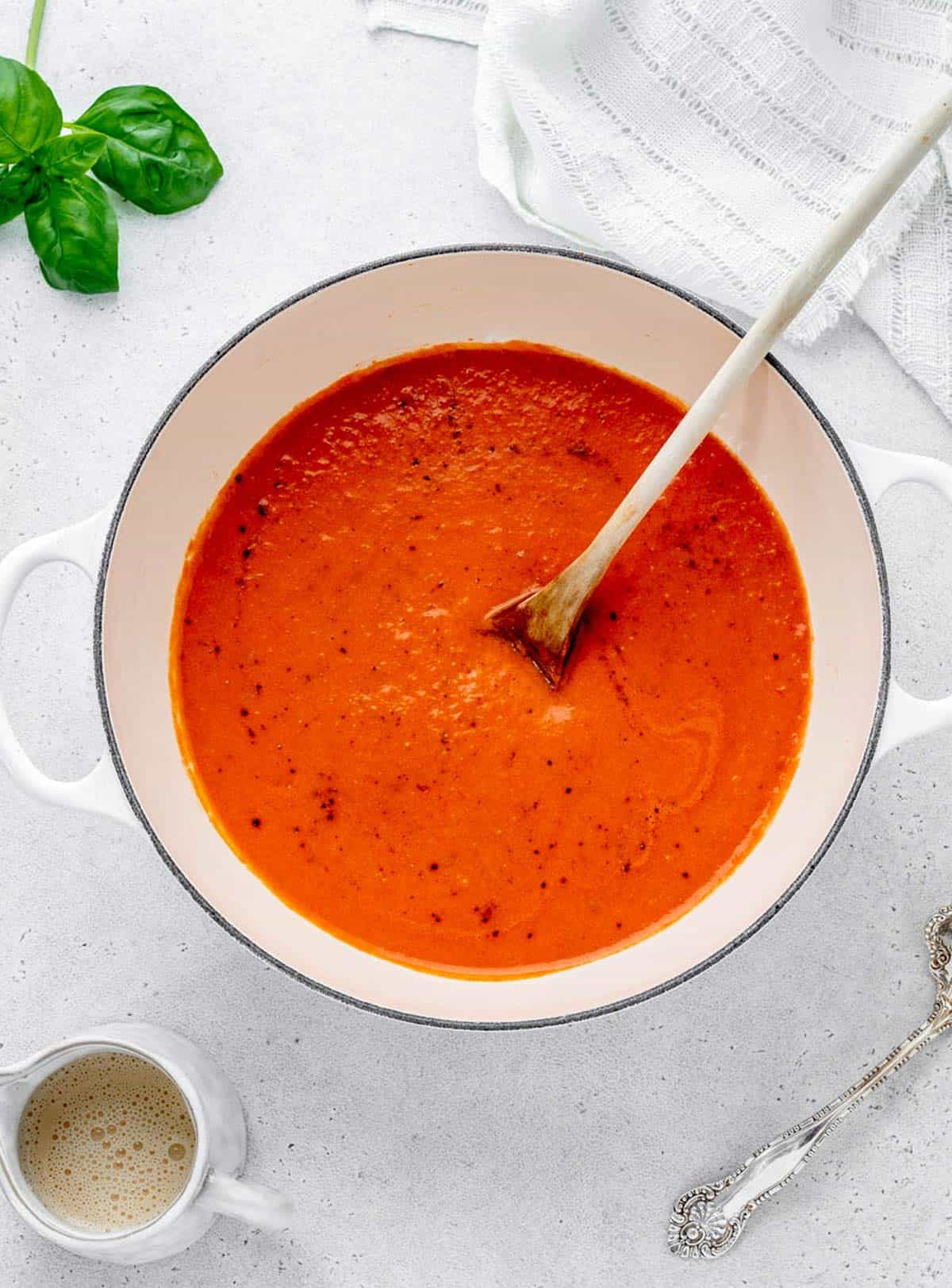 Homemade creamy tomato soup in a saucepan with a wooden spoon.