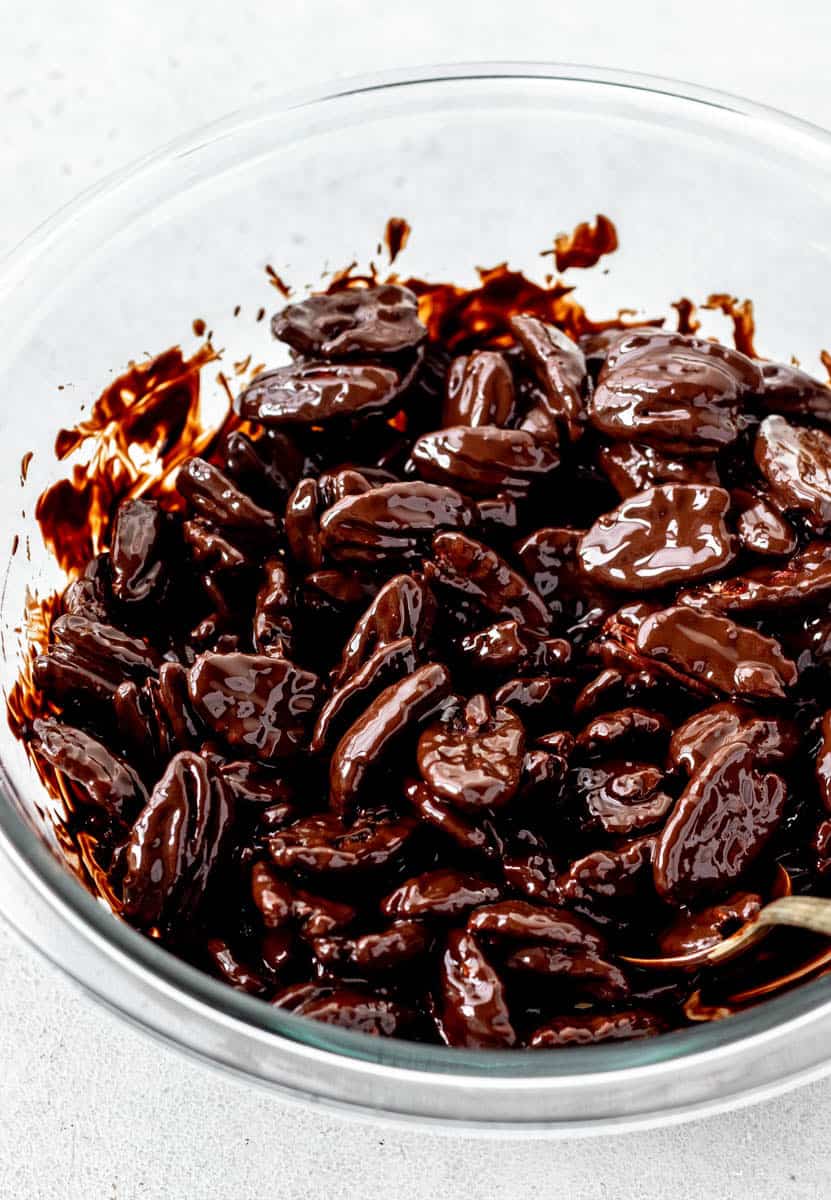 A bowl of roasted pecans being stirred into melted dark chocolate.