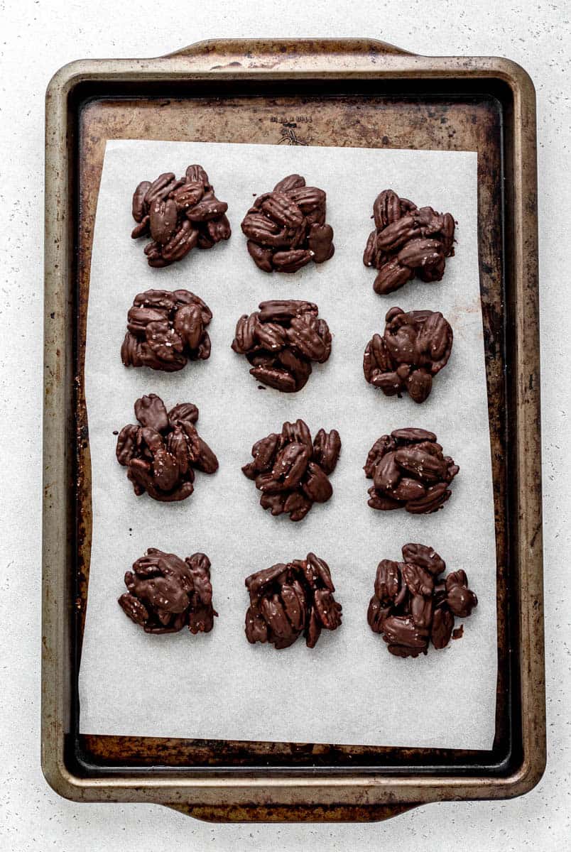 12 dark chocolate pecan clusters on a parchment lined baking sheet.