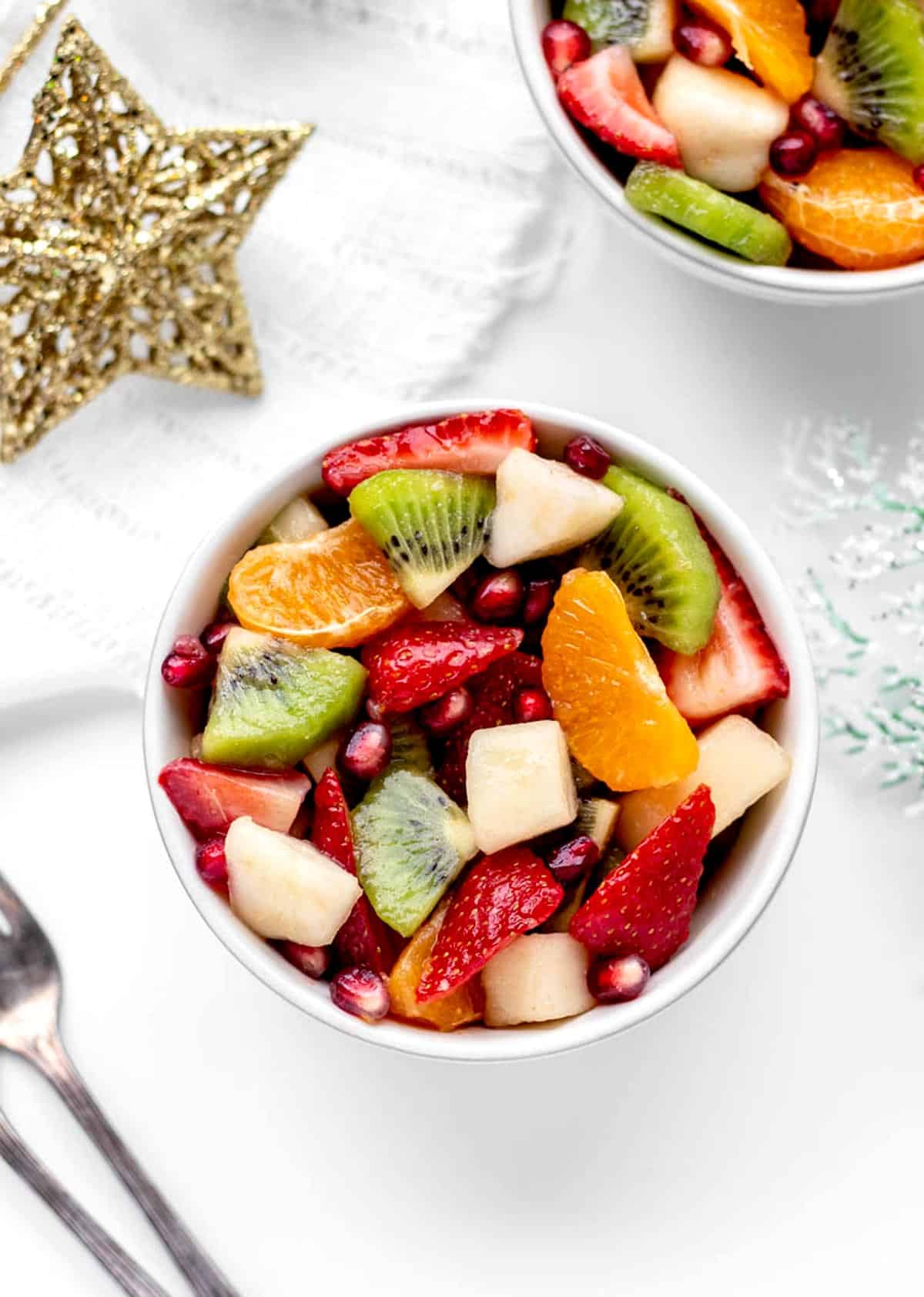 A small white bowl of winter fruit salad on a white tablecloth.