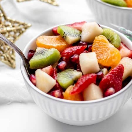 A small white serving bowl, of fruit salad with orange juice.