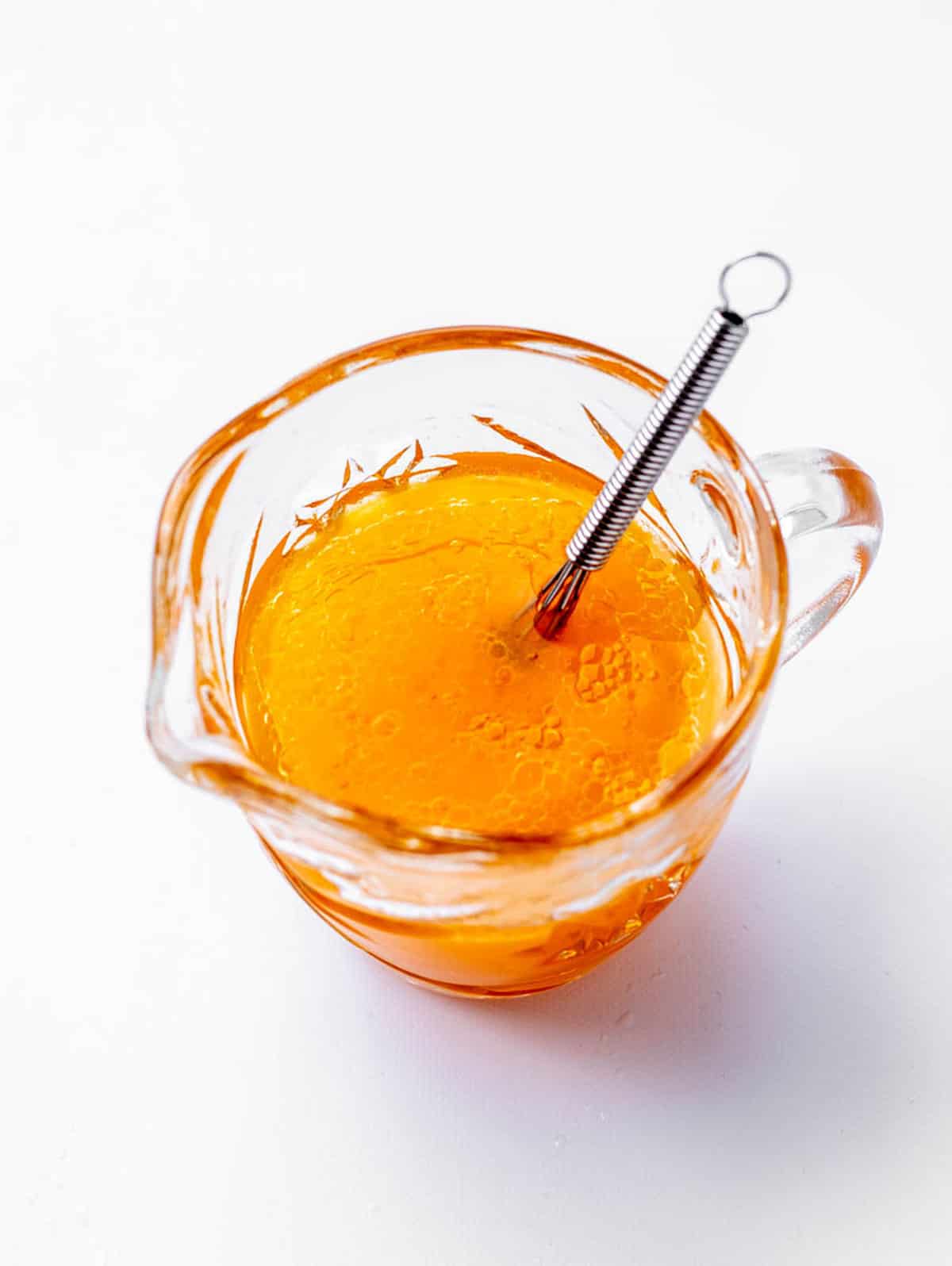 A pouring container of the dressing for holiday fruit salad, with a small whisk.