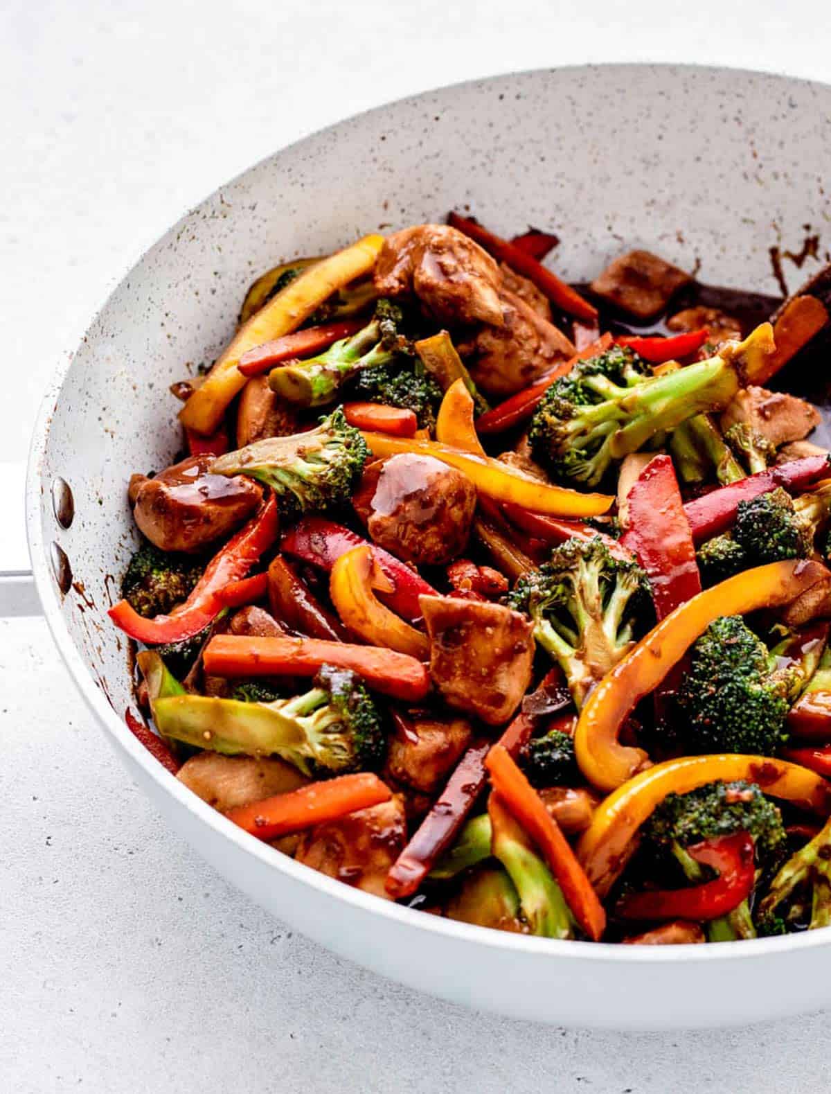 Healthy chicken and vegetable stir fry in a white frying pan.