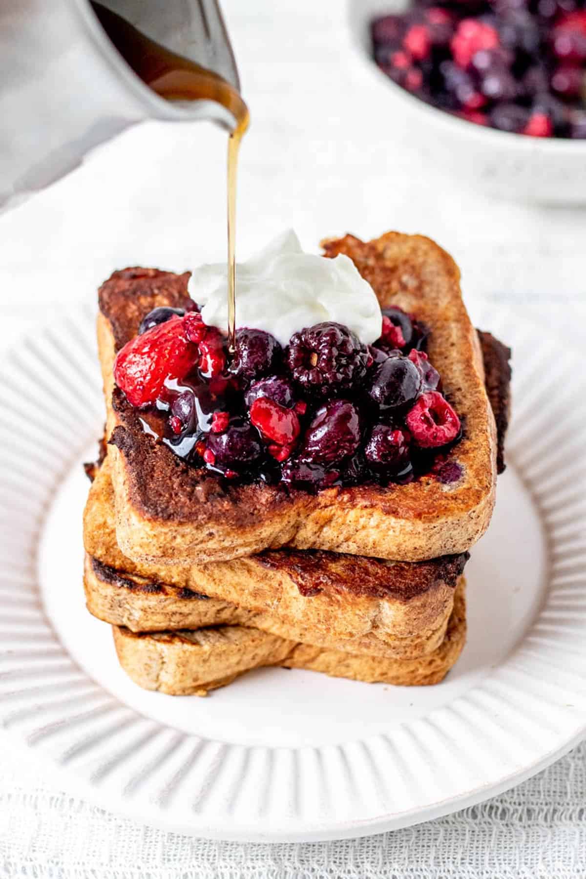 A stack of protein French toast topped with berries, Greek yogurt and poured maple syrup.