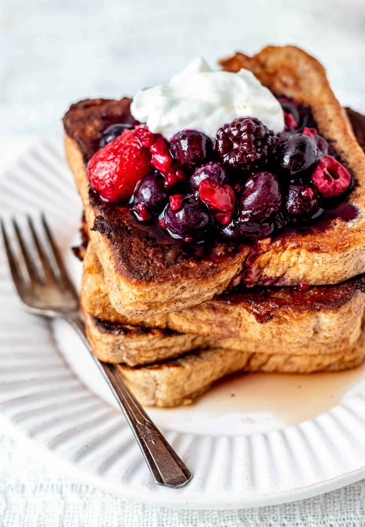 Protein French toast on a white plate, topped with mixed berries, Greek yogurt and maple syrup.