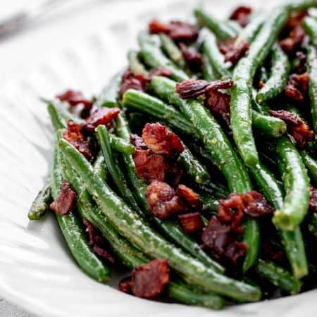A closeup of seasoned green beans and bacon on a white plate.