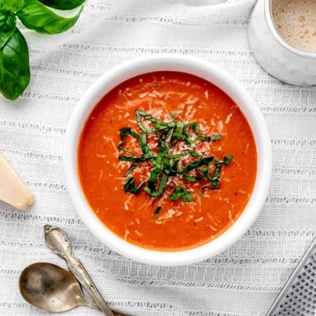A white bowl with 3 ingredient tomato soup with freshly grated parmesan and basil.