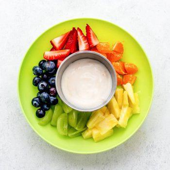 A variety of fruit served around the yogurt fruit dip in a green bowl.