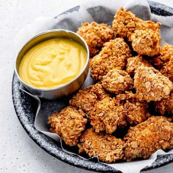 A serving plate of air fryer boneless chicken nuggets with a small bowl of dip.