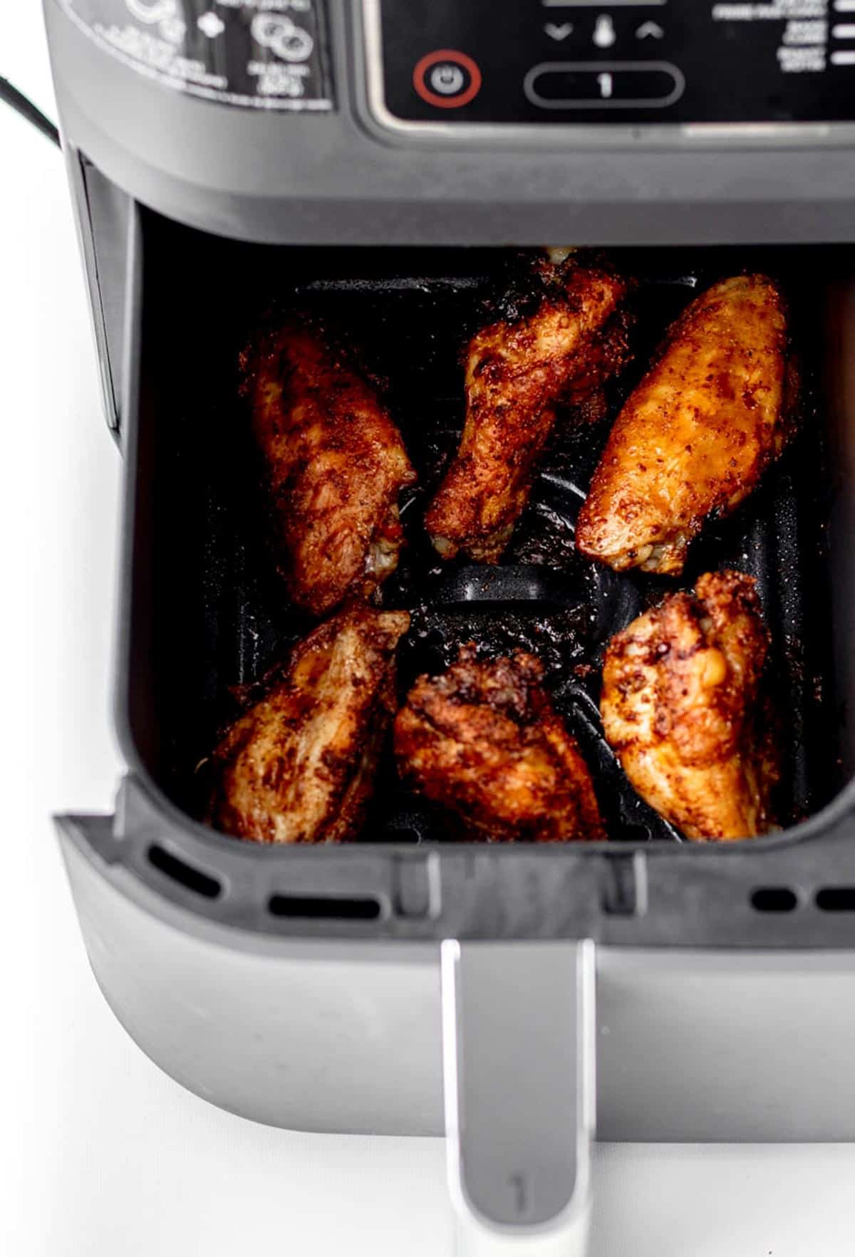 An open air fryer basket with dry rubbed chicken wings.