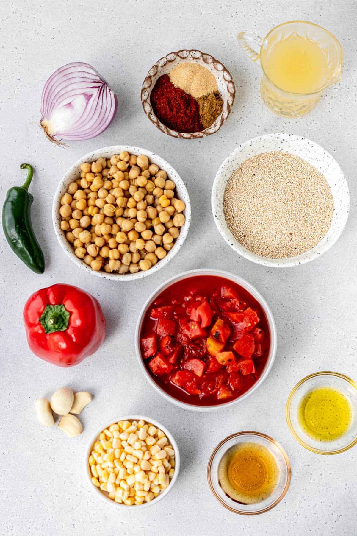 Ingredients for Mexican garbanzo soup, including garlic cloves, corn, maple syrup, fire roasted tomatoes, vegetables, vegetable broth, chickpeas, quinoa and seasonings.