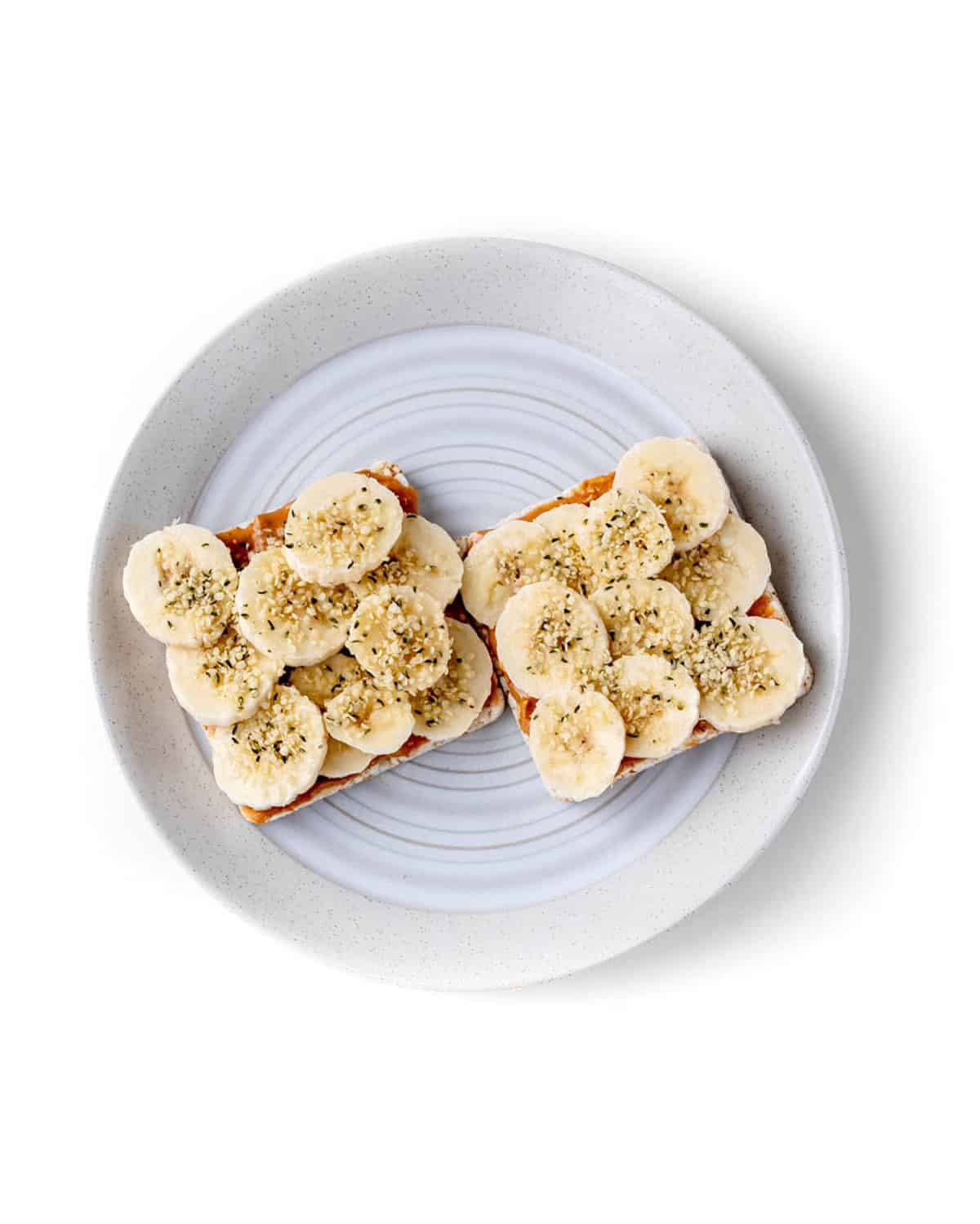 Peanut butter, banana and hemp hearts on two rice cakes on a plate.