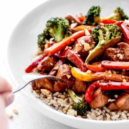 A fork poking into a bowl of easy healthy chicken stir fry, served over rice.
