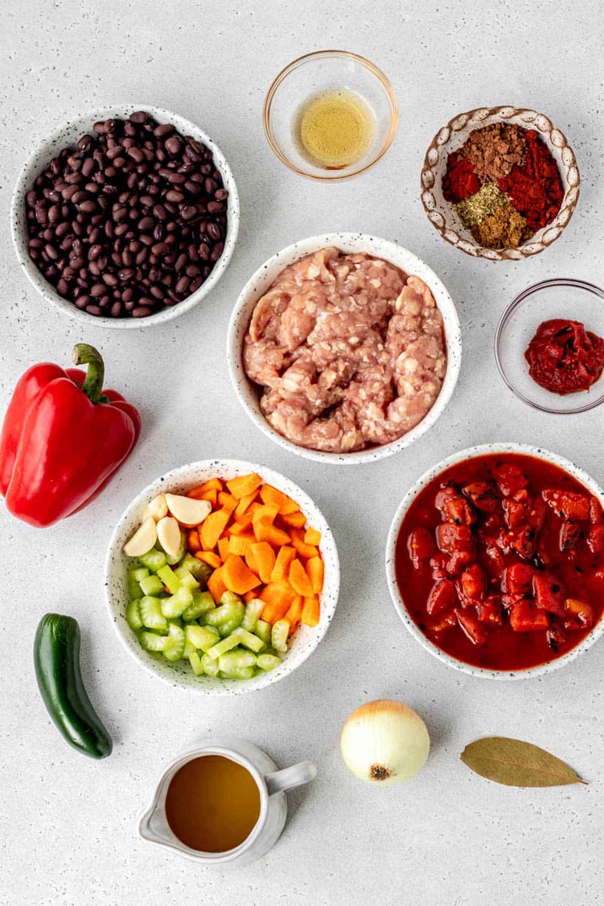 The ingredients for one pot turkey chili, including black beans, ground turkey, olive oil, spices, tomato paste, jalapeno, garlic, carrot, celery, chicken broth, onion, bay leaf and fire roasted tomatoes.