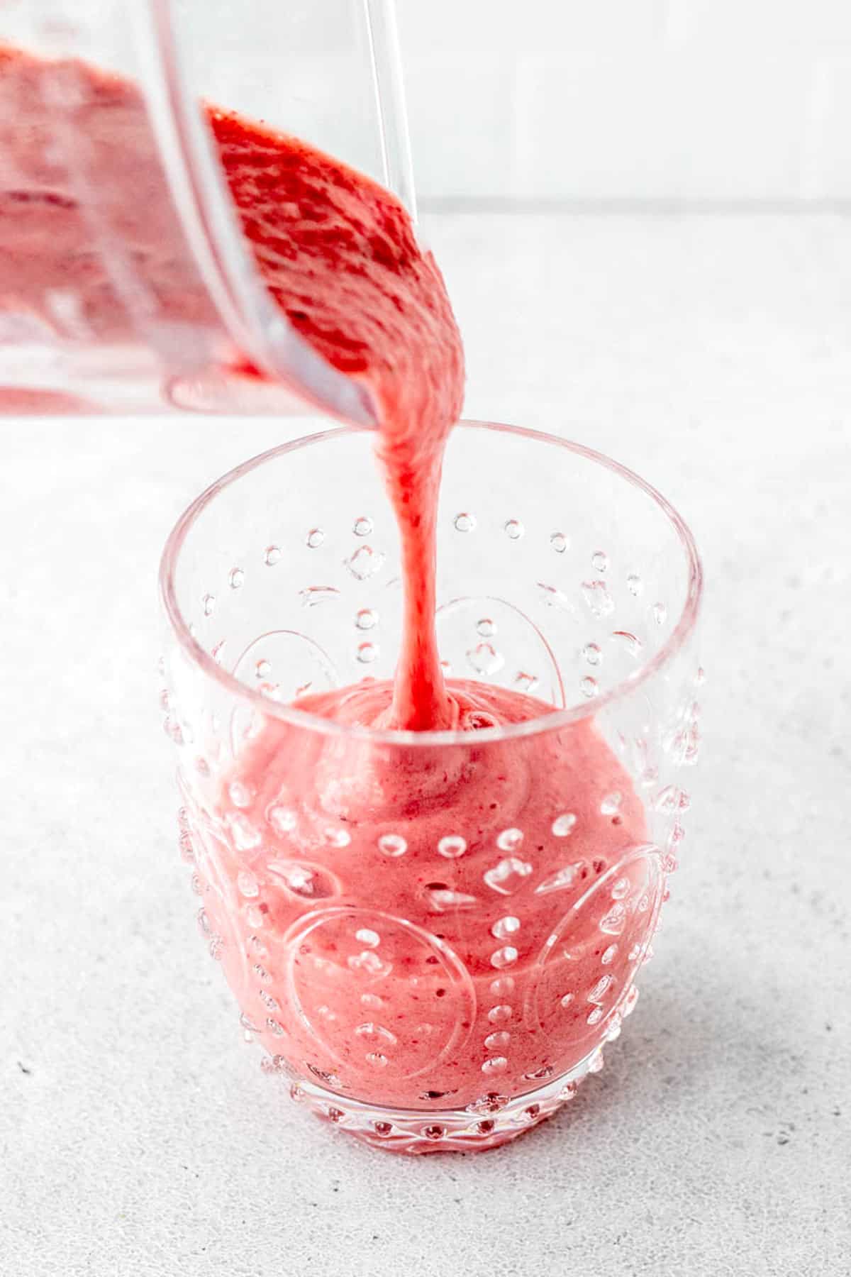 A strawberry and banana smoothie being poured into a glass.