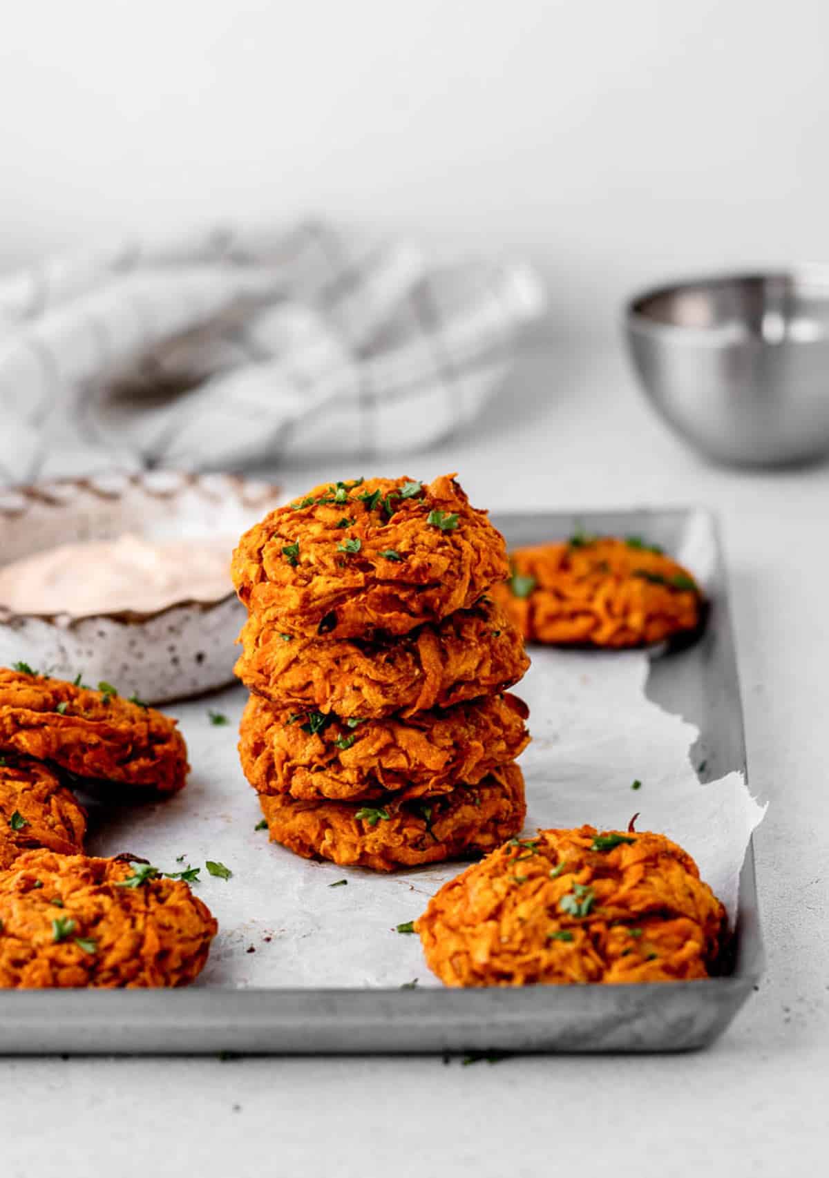 A stack of baked sweet potato fritters on a baking sheet with other fritters around it.