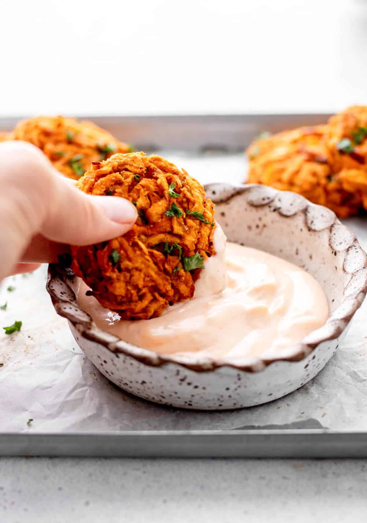 A baked sweet potato fritter being dipped into a bowl of creamy sauce.