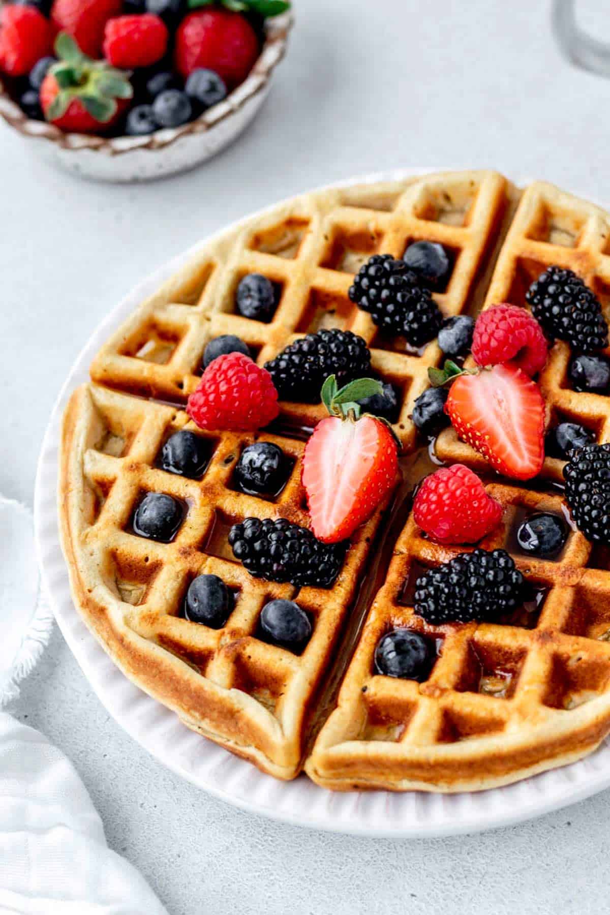A protein waffle with cottage cheese, topped with mixed berries on a white plate.