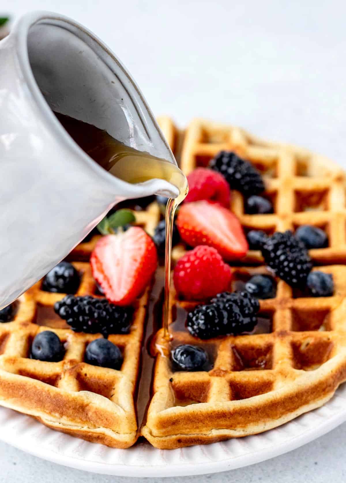 A high protein waffle with blueberries, strawberries and blackberries with maple syrup poured on it.