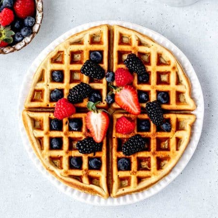A high protein waffle with mixed berries on a white plate.