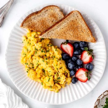 A top down view of scrambled eggs, fresh berries and toast on a white plate.