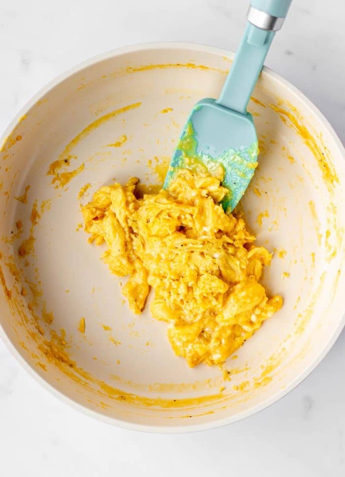 A nonstick frying pan with half cooked soft scrambled eggs, being pushed with a rubber spatula.