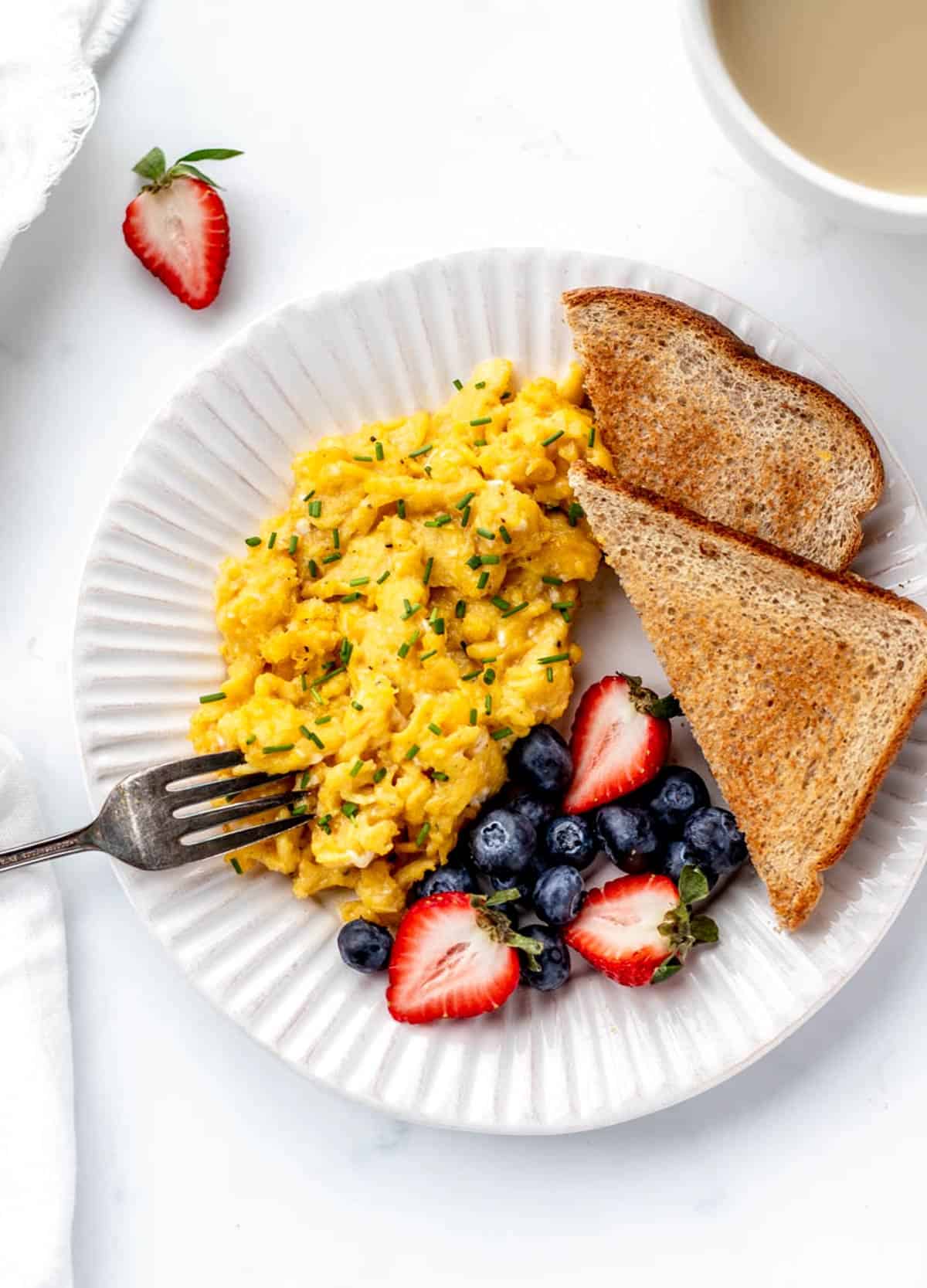 A white plate with healthy soft scrambled eggs, fresh berries and toast.