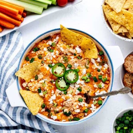 Healthier buffalo chicken dip in a serving dish with tortilla chips and a spoon dipped in.