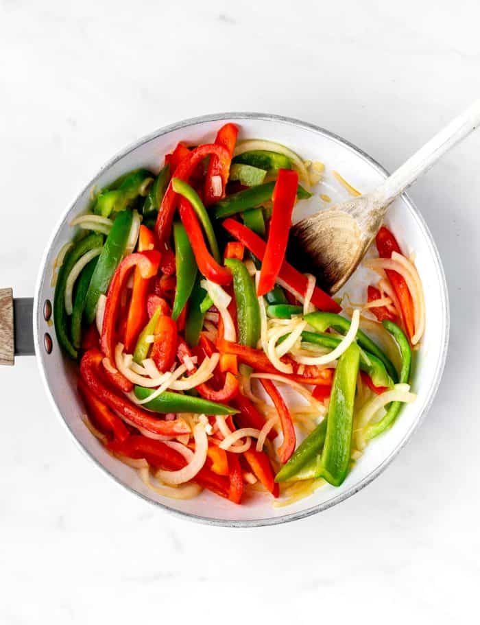 A pan of red and green bell pepper strips and onion cooking in olive oil.