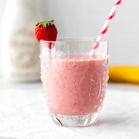 A glass of healthy strawberry banana smoothie with a straw and strawberry garnish.