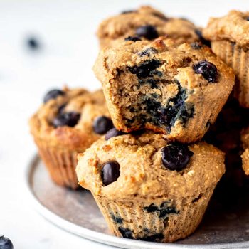 Close up image of blueberry protein muffins stacked on a tray with bite taken out of muffin.