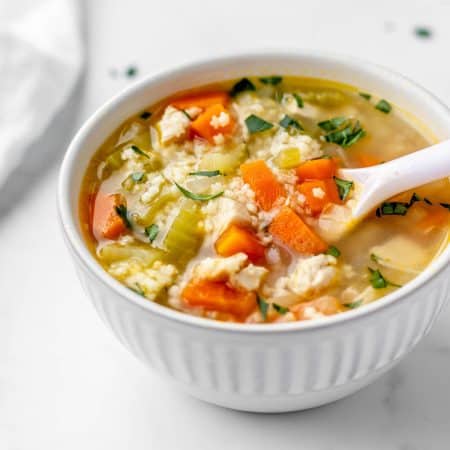 Chicken pastina soup in a bowl with a spoon scooping up some soup.