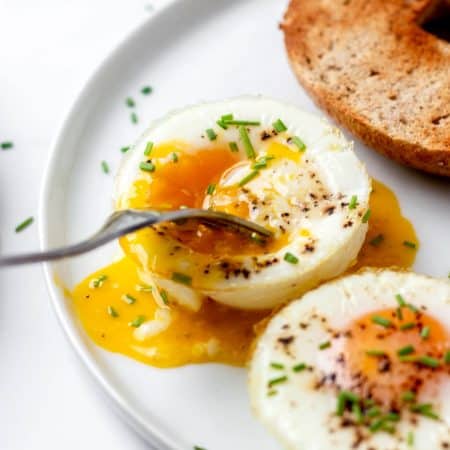 Two baked eggs on a plate with a fork poking into the runny yolk.