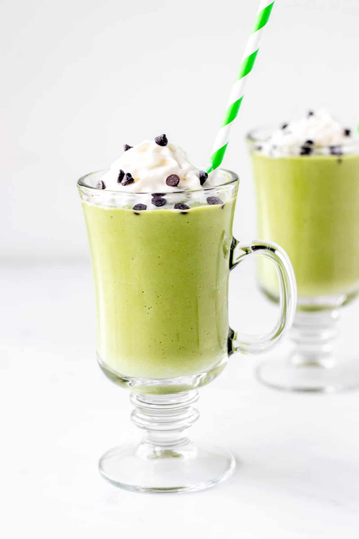 Close up image of a healthy shamrock shake topped with whip cream and chocolate chips.