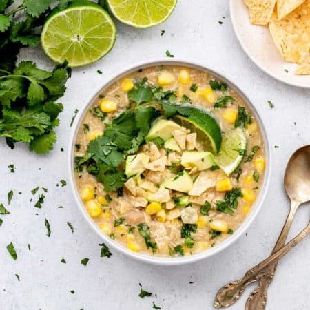 Salsa verde white chicken chili in a bowl topped with lime, cilantro, corn chips and avocado.