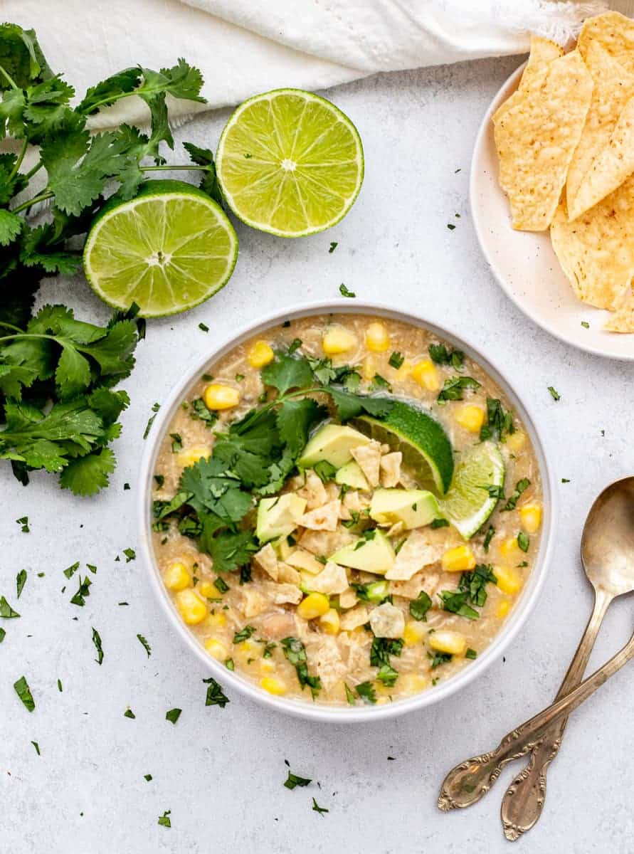 Bowl of white chicken chili with salsa verde topped with corn chips, cilantro and avocado.