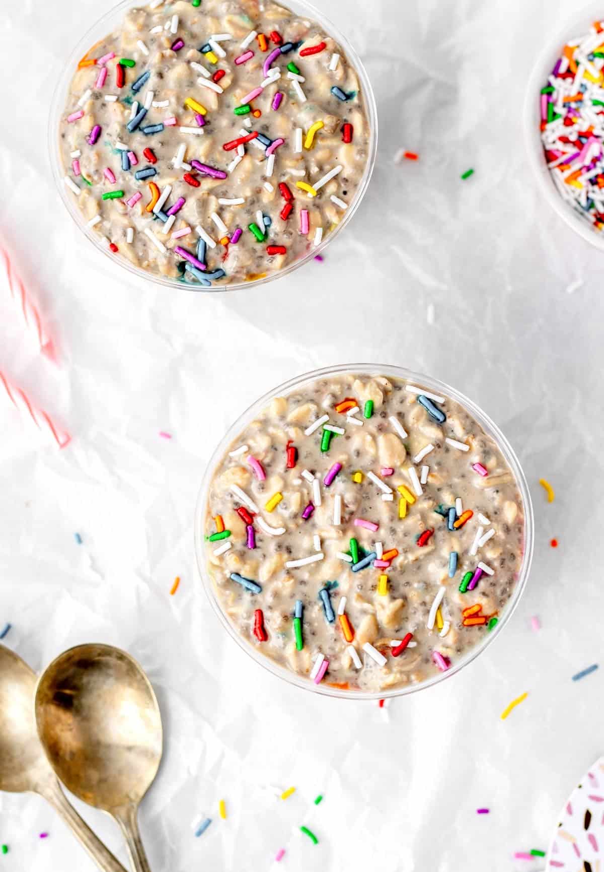 Overhead image of two cups filled with cake batter overnight oats topped with sprinkles.