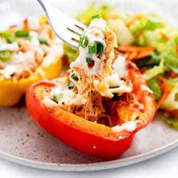 A close up image of buffalo chicken stuffed peppers with a fork holding up some chicken and cheese.